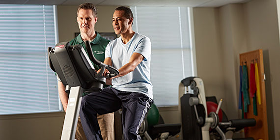 A man works with a therapist on a stationary bicycle